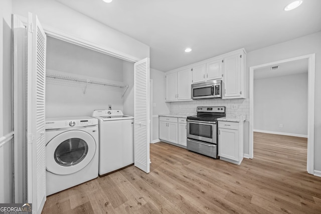 clothes washing area with washing machine and clothes dryer and light hardwood / wood-style flooring