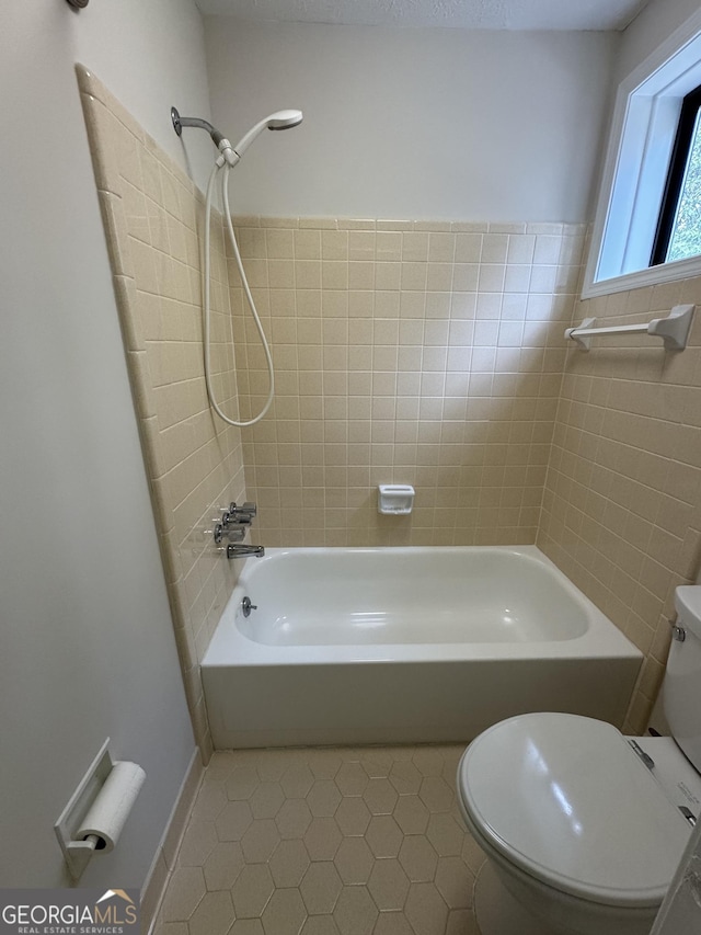 bathroom featuring tiled shower / bath, toilet, and tile patterned flooring