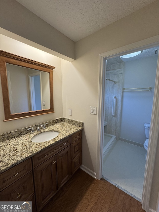 bathroom with toilet, a shower, a textured ceiling, vanity, and hardwood / wood-style flooring