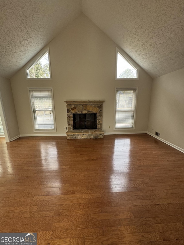 unfurnished living room featuring hardwood / wood-style flooring, a stone fireplace, high vaulted ceiling, and a textured ceiling