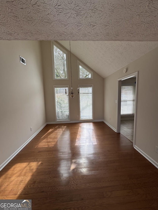 empty room featuring high vaulted ceiling, dark wood-type flooring, a chandelier, and a textured ceiling