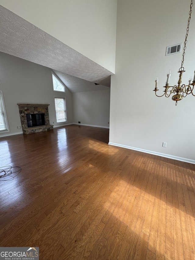 unfurnished living room featuring high vaulted ceiling, dark hardwood / wood-style floors, a notable chandelier, a textured ceiling, and a stone fireplace