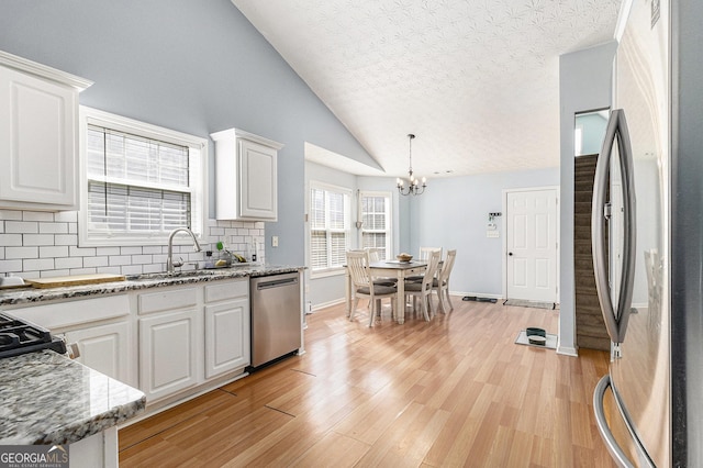 kitchen featuring light wood finished floors, appliances with stainless steel finishes, white cabinets, and pendant lighting