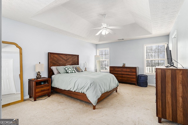 bedroom featuring baseboards, light colored carpet, ceiling fan, a tray ceiling, and a textured ceiling