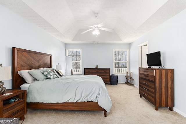 bedroom with a tray ceiling, light colored carpet, a ceiling fan, a textured ceiling, and baseboards