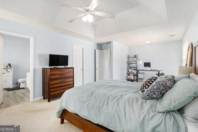 bedroom with light carpet, a tray ceiling, a textured ceiling, and ensuite bathroom