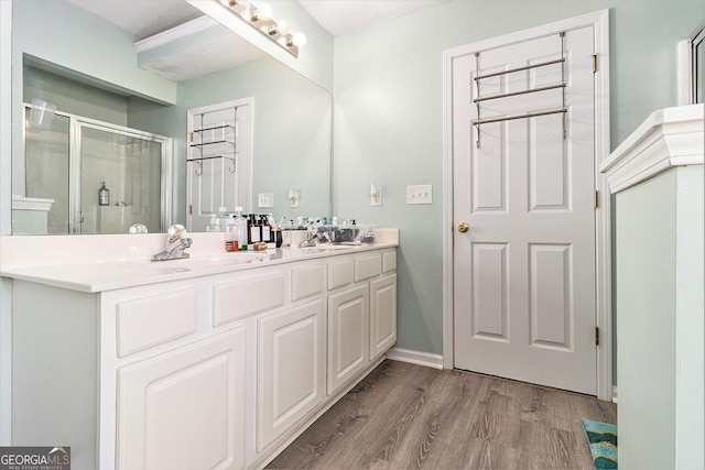 full bath with double vanity, a stall shower, a sink, wood finished floors, and baseboards