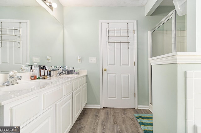 full bathroom with a stall shower, double vanity, a sink, and wood finished floors