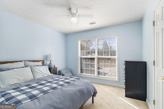 bedroom with baseboards, visible vents, light colored carpet, ceiling fan, and a textured ceiling