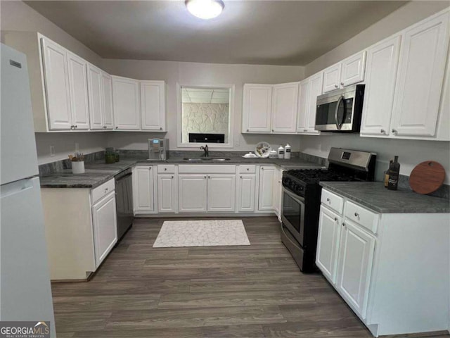 kitchen with dark wood finished floors, dark countertops, appliances with stainless steel finishes, white cabinetry, and a sink