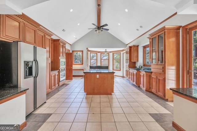 kitchen featuring stainless steel appliances, dark stone counters, beamed ceiling, and light tile patterned flooring