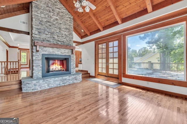 unfurnished living room featuring wood-type flooring, beam ceiling, a stone fireplace, and wooden ceiling