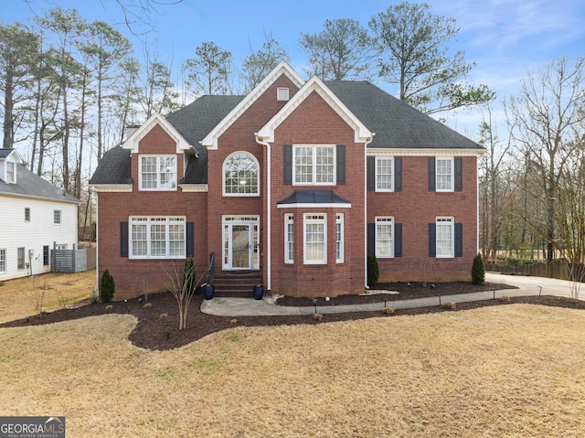 colonial home with a shingled roof, brick siding, and a front lawn