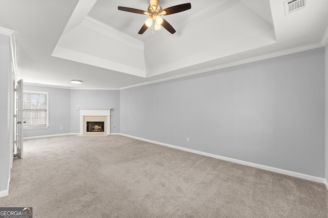 unfurnished living room with visible vents, a raised ceiling, a fireplace with flush hearth, ornamental molding, and carpet