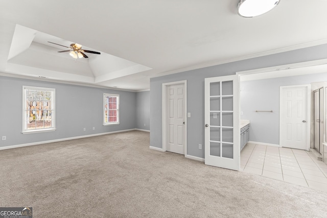 unfurnished bedroom with light tile patterned flooring, light carpet, baseboards, ornamental molding, and a tray ceiling