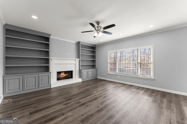 unfurnished living room featuring dark wood-style flooring, recessed lighting, ornamental molding, a brick fireplace, and baseboards