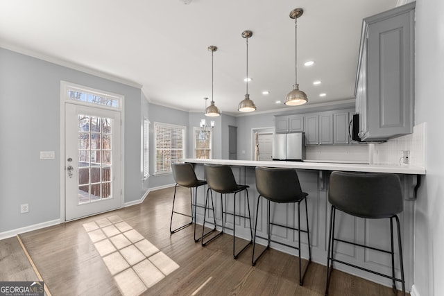 kitchen with decorative backsplash, wood finished floors, freestanding refrigerator, a peninsula, and gray cabinetry