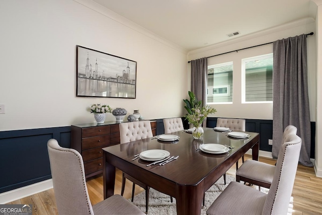 dining space with ornamental molding and light hardwood / wood-style flooring