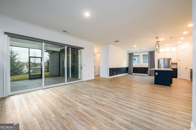 unfurnished living room with crown molding, a wealth of natural light, and light hardwood / wood-style floors