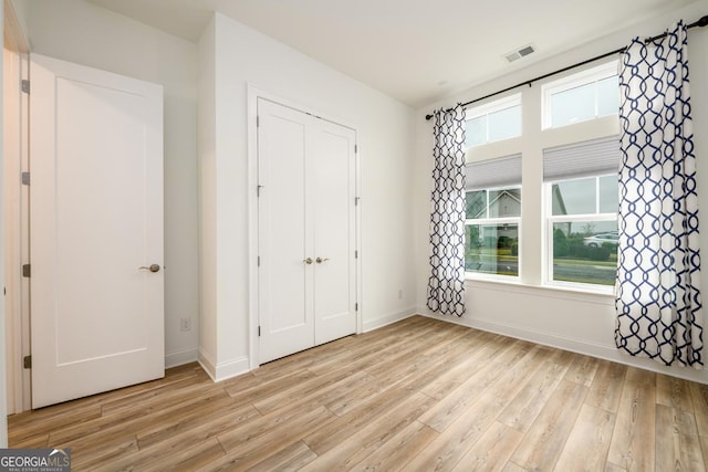 unfurnished bedroom with a closet, light hardwood / wood-style floors, and multiple windows