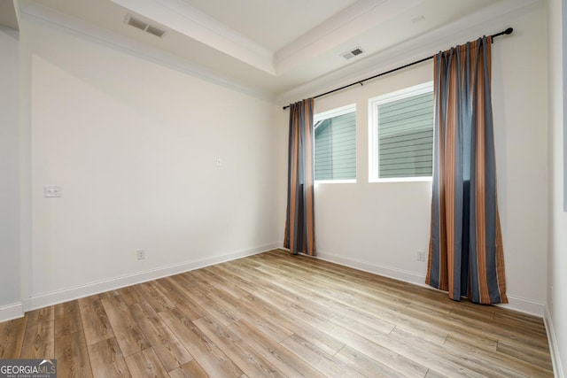 empty room featuring crown molding, light hardwood / wood-style flooring, and a tray ceiling