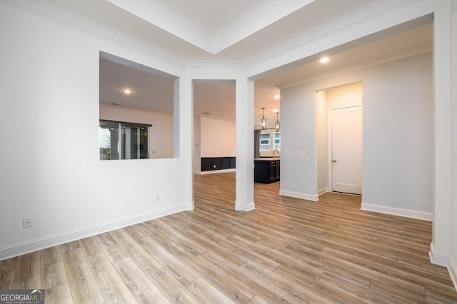 unfurnished living room featuring sink, crown molding, and light wood-type flooring