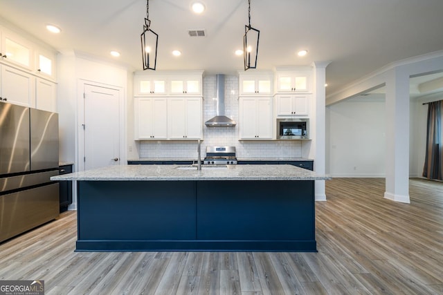 kitchen with stainless steel appliances, light stone counters, white cabinets, a center island with sink, and wall chimney exhaust hood