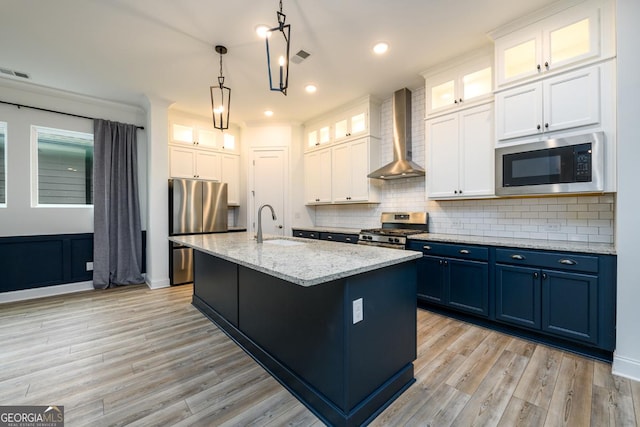 kitchen with blue cabinetry, wall chimney exhaust hood, white cabinetry, an island with sink, and stainless steel appliances