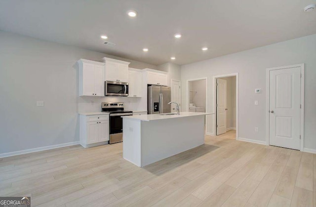 kitchen with an island with sink, light wood-style flooring, stainless steel appliances, light countertops, and a sink