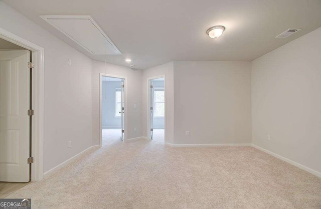 empty room with attic access, light carpet, visible vents, and baseboards