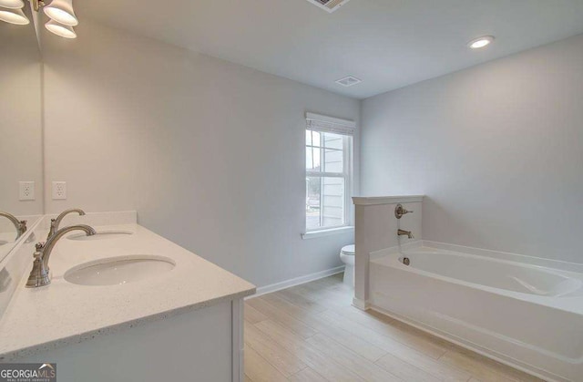 bathroom with double vanity, toilet, a bath, wood finished floors, and a sink