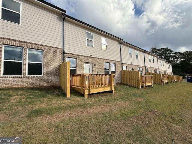 rear view of house featuring brick siding, a lawn, and a deck