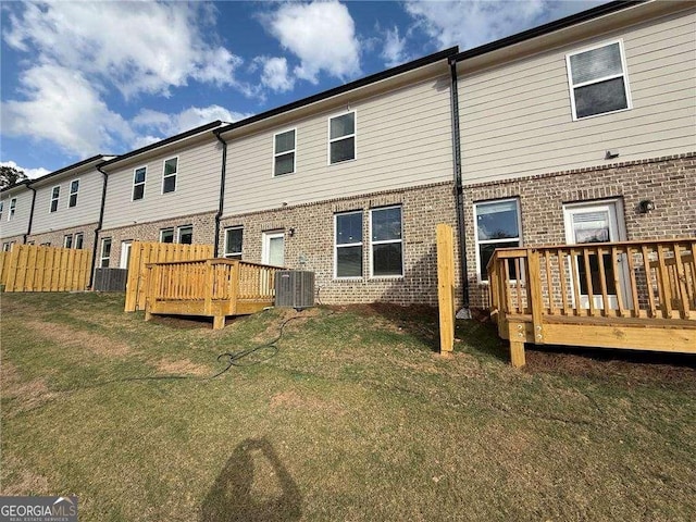 rear view of property with a yard, brick siding, a wooden deck, and fence