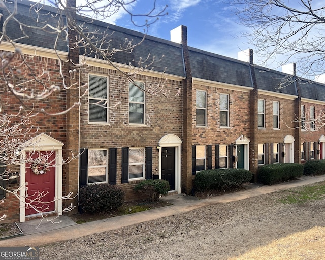 view of front of property with a shingled roof, a chimney, mansard roof, and brick siding