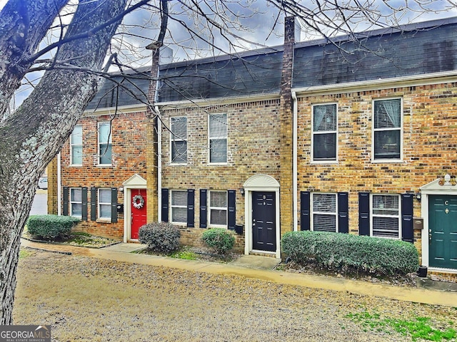 view of property featuring roof with shingles, brick siding, and a chimney