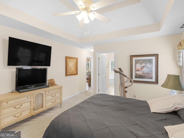 bedroom with ceiling fan, light colored carpet, ensuite bathroom, and a raised ceiling