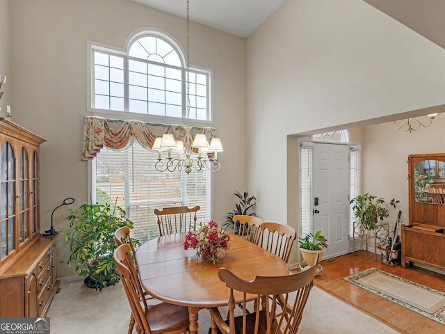 dining space with light wood-type flooring, a healthy amount of sunlight, high vaulted ceiling, and a notable chandelier