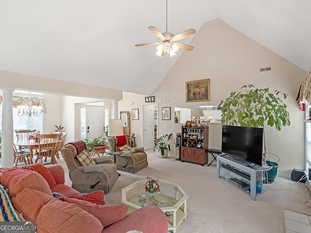 living room featuring decorative columns, ceiling fan with notable chandelier, light colored carpet, and high vaulted ceiling