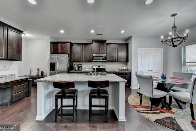 kitchen with pendant lighting, dark brown cabinetry, stainless steel appliances, and an island with sink