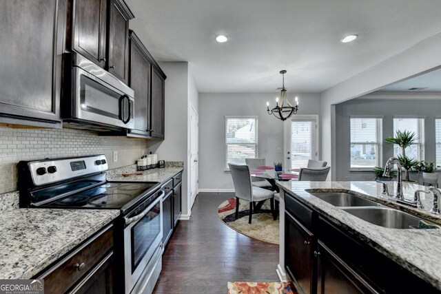 kitchen featuring dark brown cabinetry, sink, hanging light fixtures, appliances with stainless steel finishes, and light stone countertops