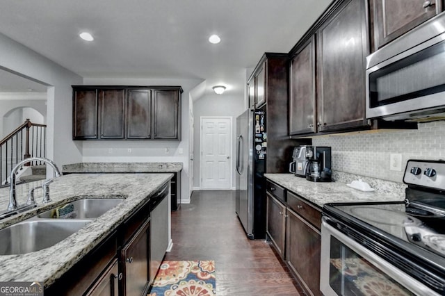 kitchen with appliances with stainless steel finishes, sink, decorative backsplash, dark brown cabinetry, and light stone counters