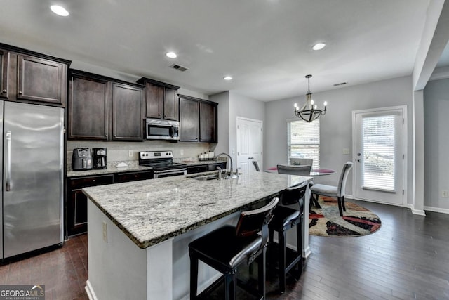 kitchen featuring pendant lighting, an island with sink, sink, stainless steel appliances, and light stone countertops