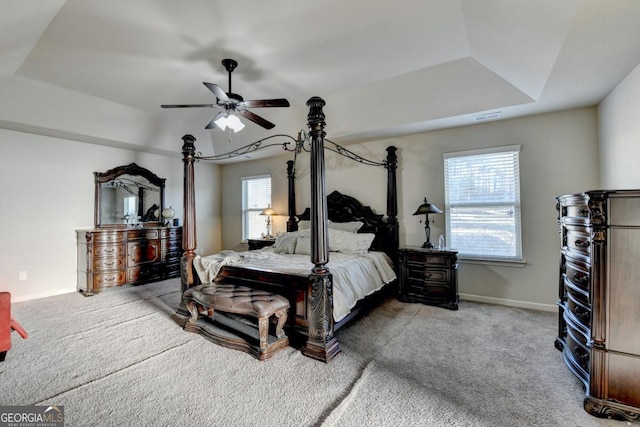 carpeted bedroom with a raised ceiling and ceiling fan