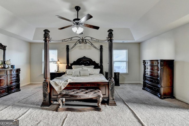 carpeted bedroom with a raised ceiling and ceiling fan