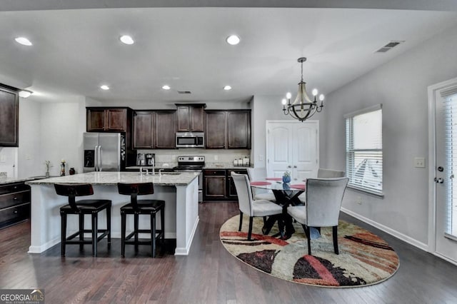 kitchen with a kitchen island with sink, hanging light fixtures, stainless steel appliances, a kitchen breakfast bar, and dark brown cabinetry