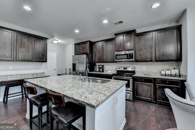 kitchen featuring dark wood-type flooring, a kitchen bar, sink, an island with sink, and stainless steel appliances