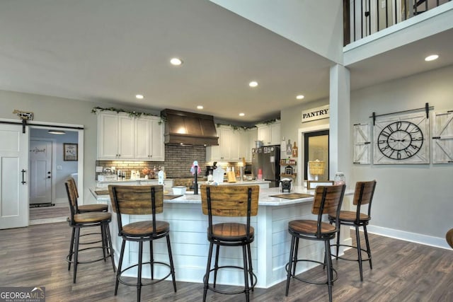 kitchen featuring premium range hood, a breakfast bar area, an island with sink, a barn door, and white cabinets