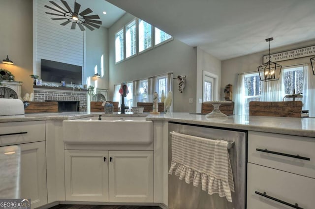 kitchen with sink, dishwasher, white cabinetry, a brick fireplace, and decorative light fixtures