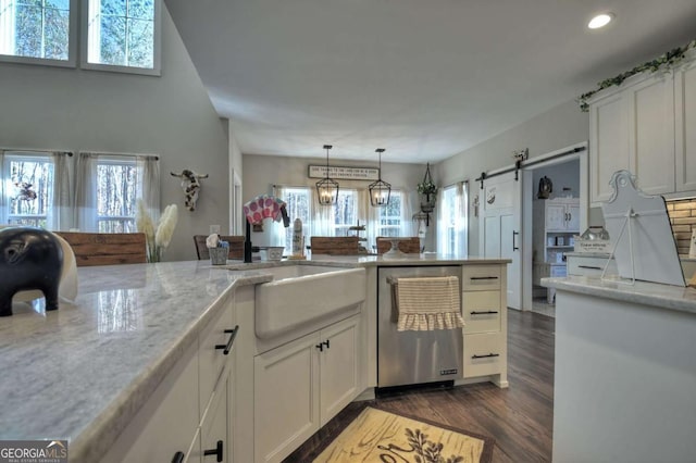 kitchen with pendant lighting, white cabinetry, dishwasher, light stone counters, and a barn door