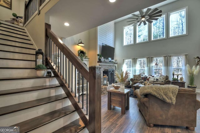 living room with a high ceiling, dark hardwood / wood-style floors, a fireplace, and ceiling fan